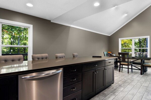 A kitchen with a large island, dark cabinetry, and a view of trees through the windows. - Schuss Mountain Chalet (Mancelona)