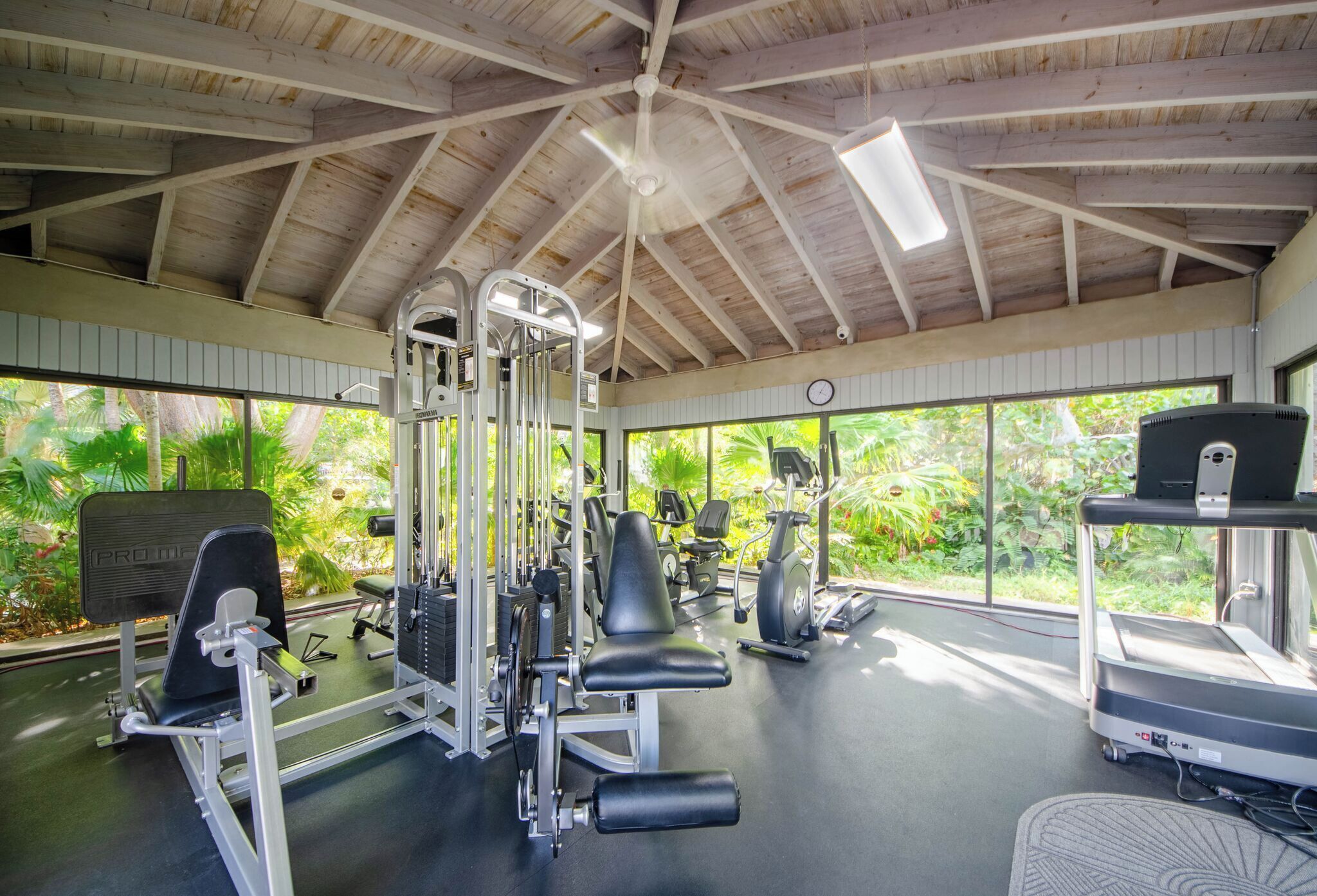 Une salle de sport équipée de divers appareils d’exercice, dotée de grandes fenêtres et d’un plafond en bois.