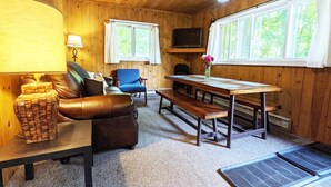A cozy cabin interior with a leather sofa, a blue armchair, a wooden dining table, and a bench.
