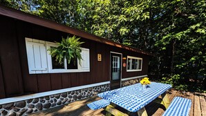A wooden deck with a picnic table and benches, surrounded by a stone wall and a wooden building with white shutters.