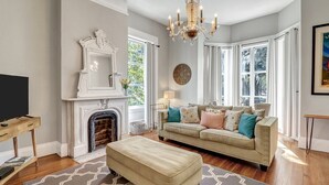 A living room with a fireplace, a sofa, an ottoman, and a television. - Mayor's luxury 1869 historic home for 4 on the square! (Savannah)