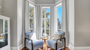 A corner room with two armchairs, a small table, and a large window with curtains. - Mayor's luxury 1869 historic home for 4 on the square! (Savannah)