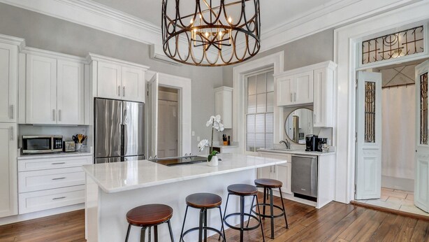 A modern kitchen with white cabinetry, stainless steel appliances, a central island with stools, and a decorative chandelier. - Mayor's luxury 1869 historic home for 4 on the square! (Savannah)
