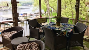 A covered outdoor seating area with wicker furniture and a table with a colorful tablecloth, overlooking a lake with boats and greenery. - Lakefront home near Margaritaville  w/lrg private dock -Kelly’s Place (Osage beach)