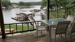 A wooden deck with a glass table and chairs overlooking a marina with docks and boats. - Lakefront home near Margaritaville  w/lrg private dock -Kelly’s Place (Osage beach)