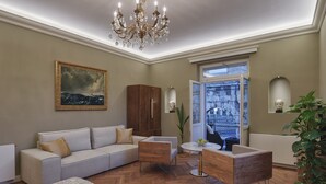 A living room with a sofa, a wooden coffee table, a chandelier, and a view of the city through a window. - Arena & Seaview Luxury Residence (Pula)