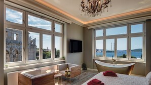 A hotel room with a large window, a bathtub, a desk, and a bed. - Arena & Seaview Luxury Residence (Pula)