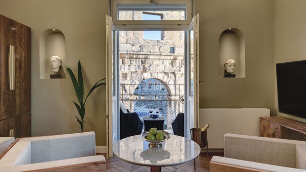 A modern living room with a round table, two sofas, a TV, and a view of a stone building through a glass door. - Arena & Seaview Luxury Residence (Pula)