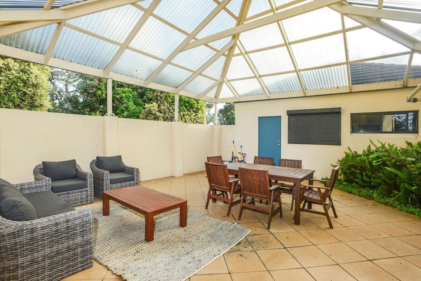 Ein überdachter Patio-Bereich mit Korbmöbeln, einem Holztisch und Stühlen.