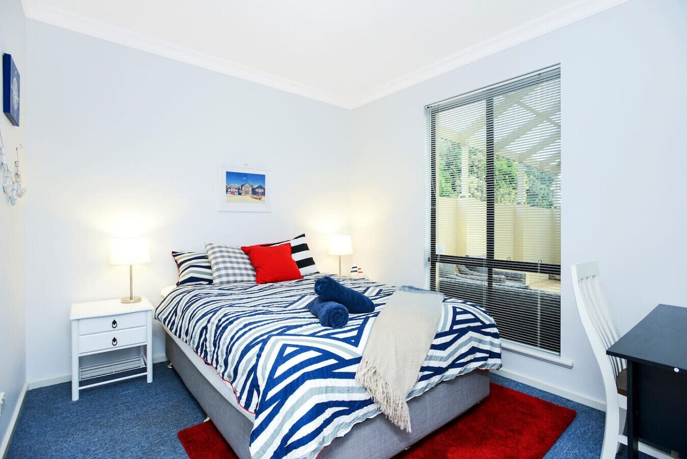 Ein Schlafzimmer mit einem Bett, zwei Nachttischen, einem Fenster mit Jalousien und einem Bild an der Wand.