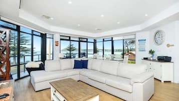 A modern living room with a large sectional sofa, a wooden coffee table, and a view of the ocean through large windows.