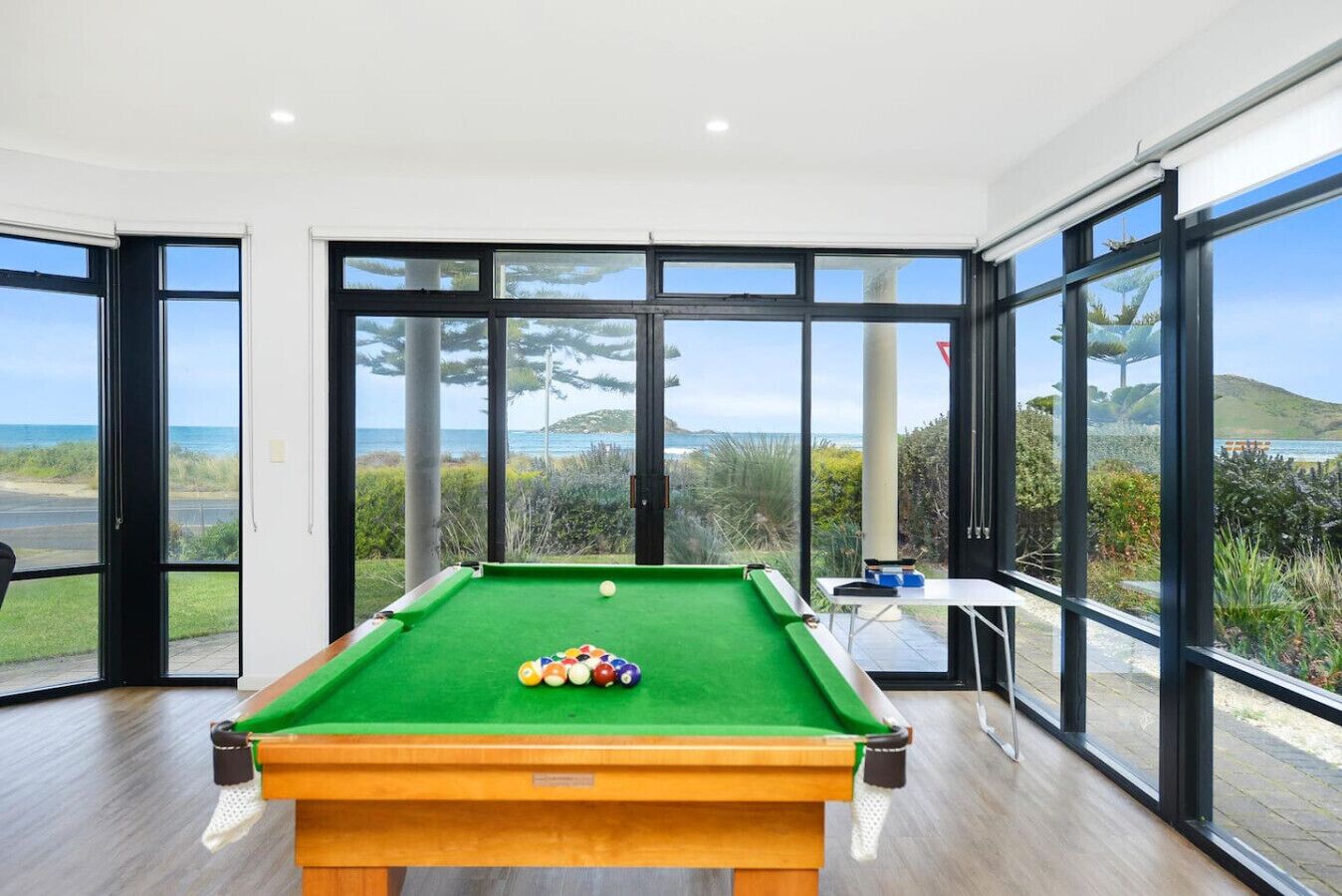 A pool table with a clear view of the ocean through large windows.