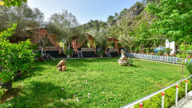 Un jardín exuberante con una fuente, cerca viva blanca y un edificio rústico de techo rojo.