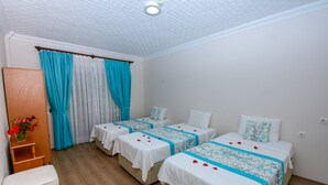 Una habitación de hotel con dos camas, un armario de madera, una mesita con un jarrón de flores y una silla.