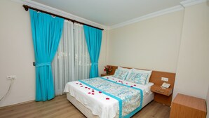 Un dormitorio con cama, mesita de noche, una mesita auxiliar de madera y cortinas.