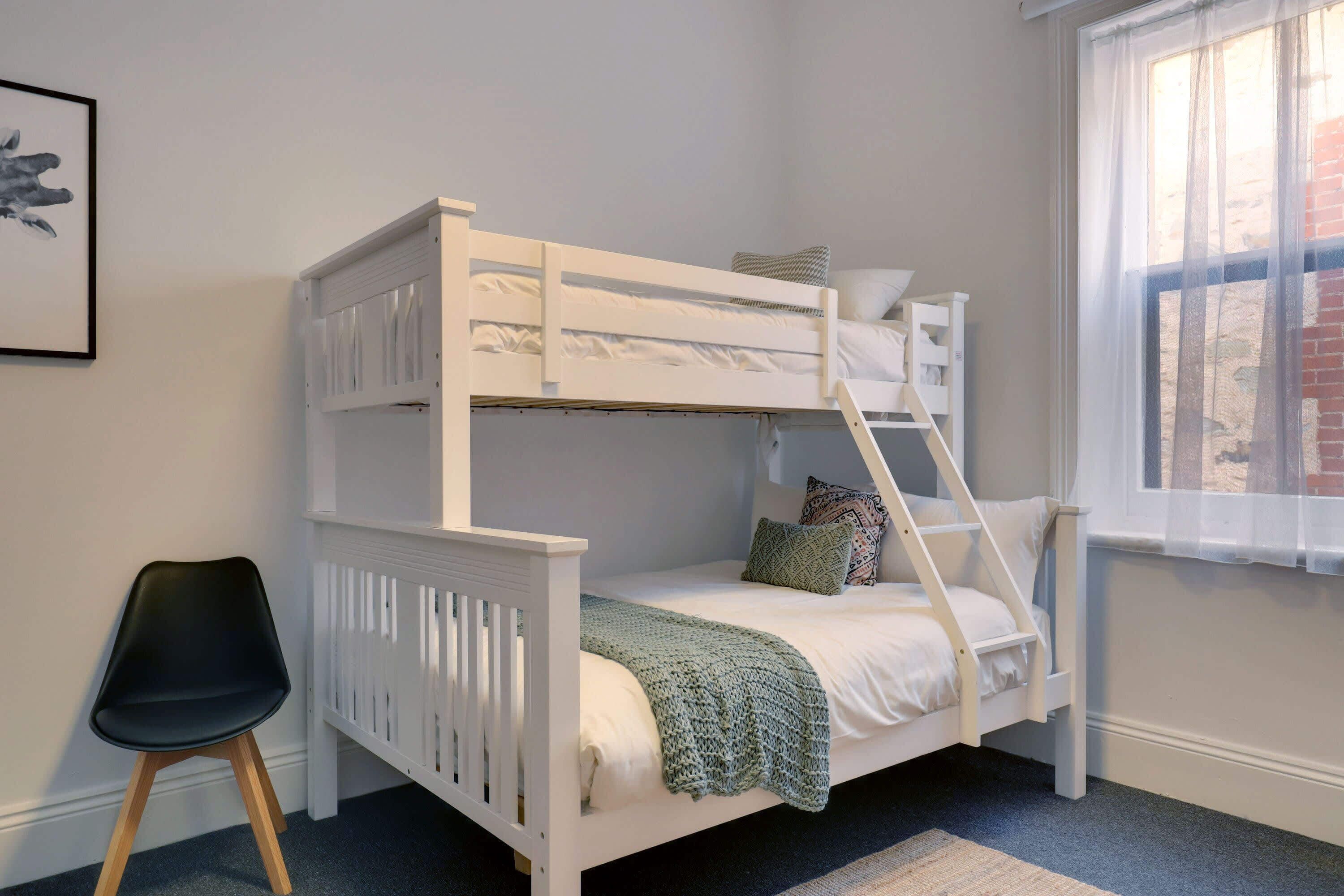 A bunk bed with a ladder, a black chair, and a window with curtains.