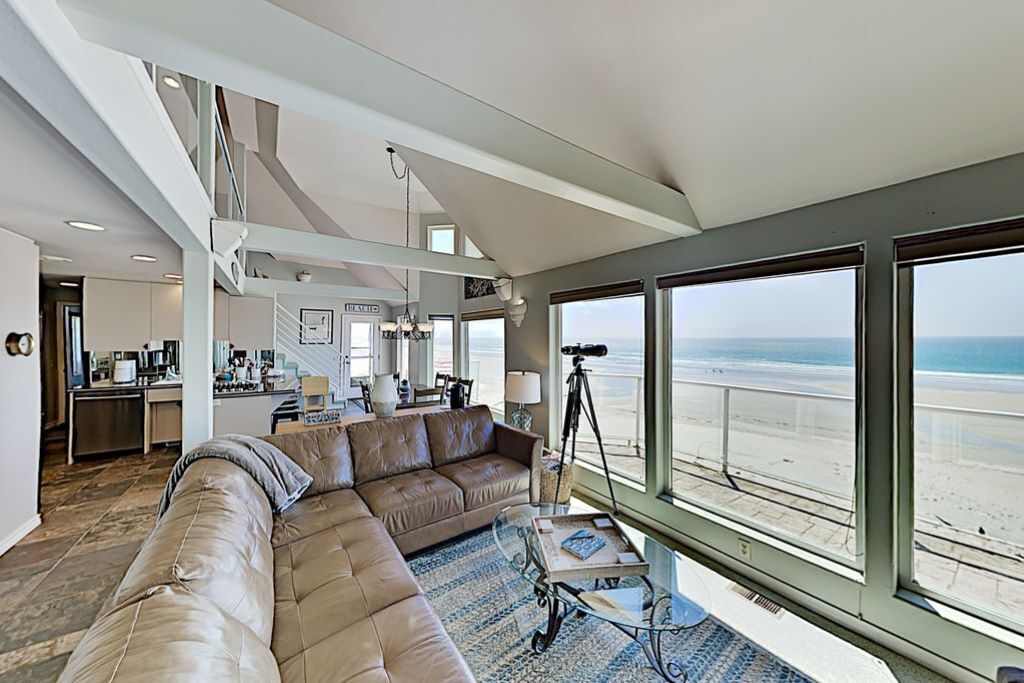 Un salon spacieux avec un grand canapé en cuir, une table basse et un télescope. La pièce est dotée de grandes fenêtres qui offrent une vue sur la plage.
