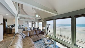 Amplia sala de estar con un gran sofá de cuero, una mesa de centro y un telescopio. La habitación tiene ventanas amplias con vistas a la playa.