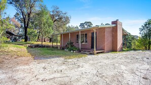 A small brick house with a porch, surrounded by trees and a dirt yard. - Braeside Cabin Two - Alphitonia (CENTRAL TILBA)