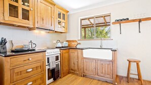 A kitchen with wooden cabinets, a stove, a sink, and a window with a view of trees. - Braeside Cabin Two - Alphitonia (CENTRAL TILBA)