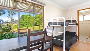 A dormitory room with bunk beds, a wooden desk, and a window overlooking greenery. - Braeside Cabin Two - Alphitonia (CENTRAL TILBA)