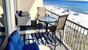 Ein Balkon mit Blick auf den Strand, einem Tisch, Stühlen und einer Korbsitzgruppe.