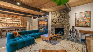 Una sala de estar moderna con chimenea de piedra, un sofá seccional azul, una mesa de centro y una estantería.