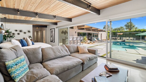 Una sala de estar moderna con un sofá grande, una mesita de centro con libros y vistas a una piscina al aire libre.