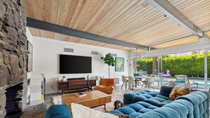 Una sala de estar moderna con chimenea de piedra, televisor grande y vista a la piscina.