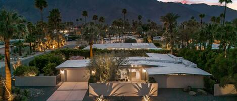 A modern resort with multiple buildings, palm trees, and a mountainous backdrop.