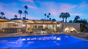 Una casa moderna con piscina, mobiliario de patio y palmeras.