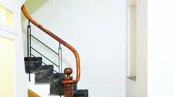 Un escalier avec une rampe en bois et des marches noires, menant à un palier avec un mur blanc et une porte.