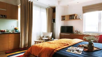 Une chambre d’hôtel comprenant un lit, une télévision, un bureau, une chaise, une fenêtre avec des rideaux et une kitchenette.