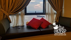 Una habitación con un ventanal amplio, un sofá con cojines rojos y vistas a un horizonte urbano distante.