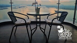 Un balcón con dos sillas y una mesa, con vistas a un cuerpo de agua y un paisaje urbano distante.