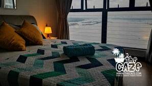 Habitación de hotel con una cama grande, una mesita de noche con lámpara y vistas a un cuerpo de agua a través del ventanal.