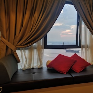 Ein Zimmer mit einem großen Fenster, einem Sofa mit roten Kissen und Blick auf eine entfernte Skyline.