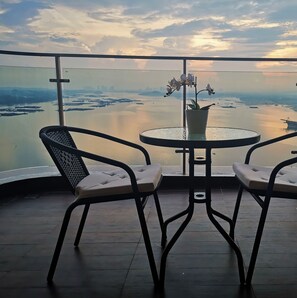 Ein Balkon mit zwei Stühlen und einem Tisch, mit Blick auf ein Gewässer und eine Stadtlandschaft in der Ferne.