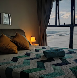 Ein Hotelzimmer mit einem großen Bett, einem Nachttisch mit Lampe und Blick auf ein Gewässer durch das Fenster.