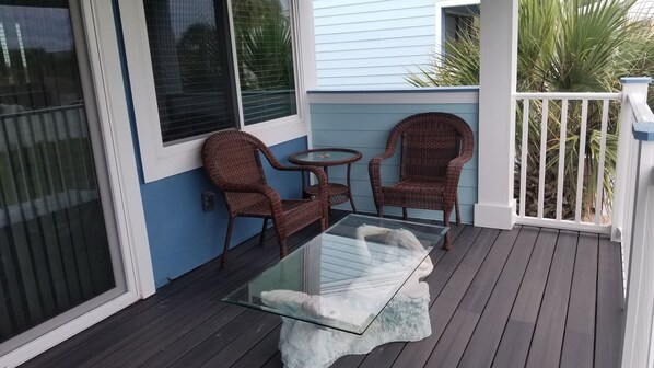 A covered porch with a glass table and wicker chairs, a small round table, and a white railing. - Cozy Relaxation on Crescent Beach (St. Augustine)