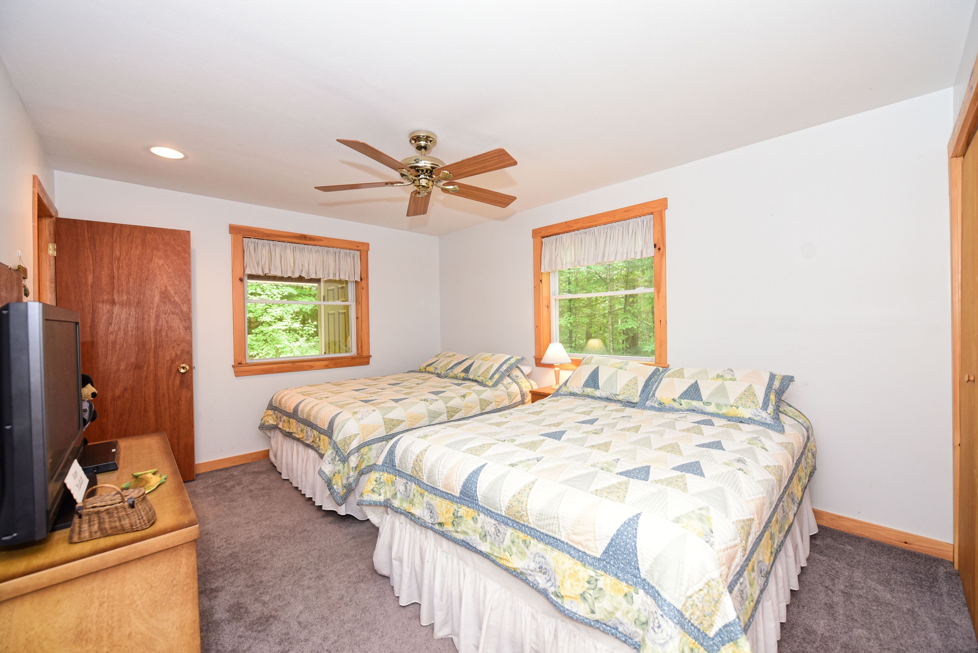 A bedroom with two beds, a ceiling fan, a TV, and a desk with a lamp.