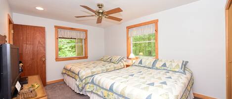 A bedroom with two beds, a ceiling fan, a TV, and a desk with a lamp.