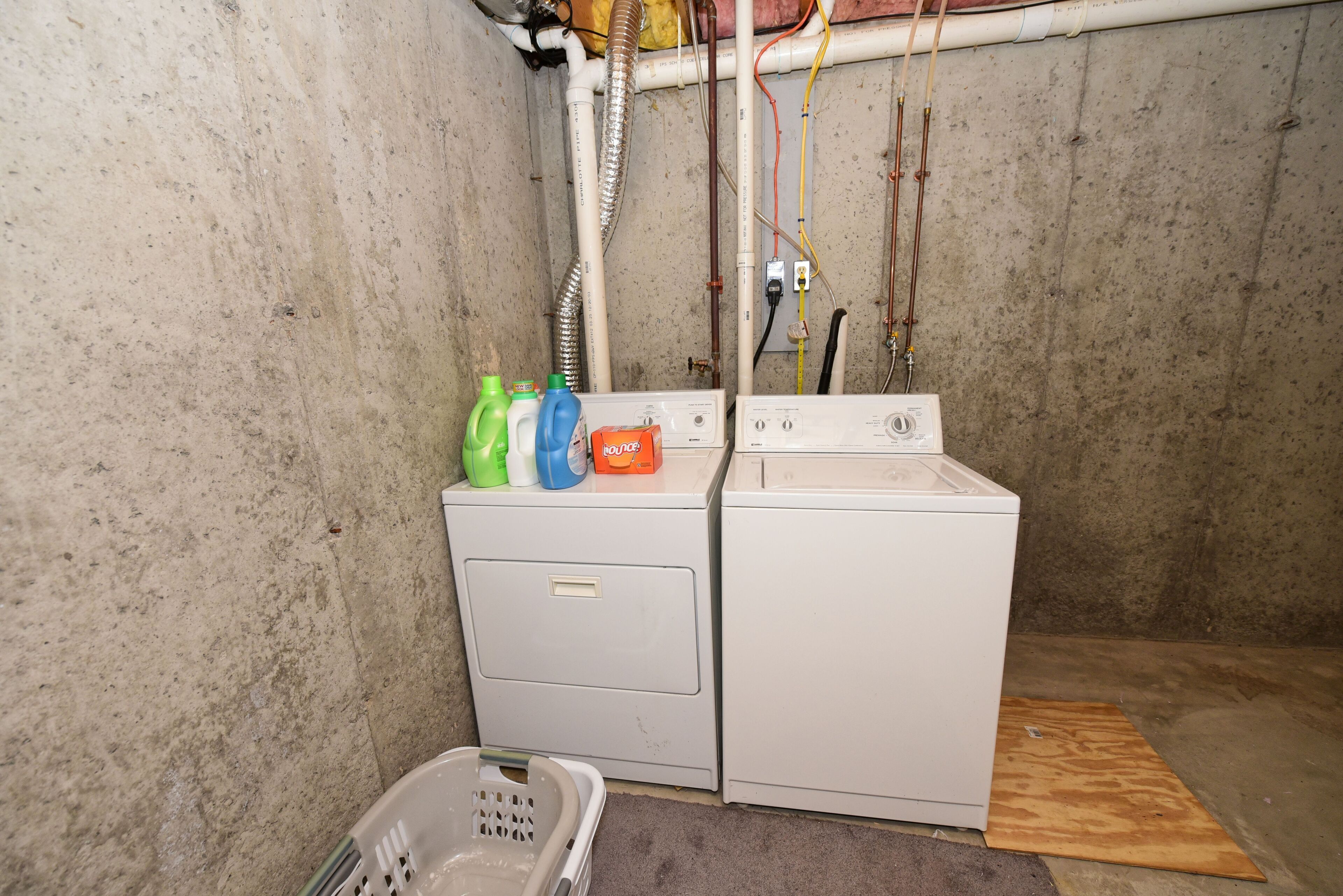 A laundry area with two washing machines, a dryer, and a laundry basket.