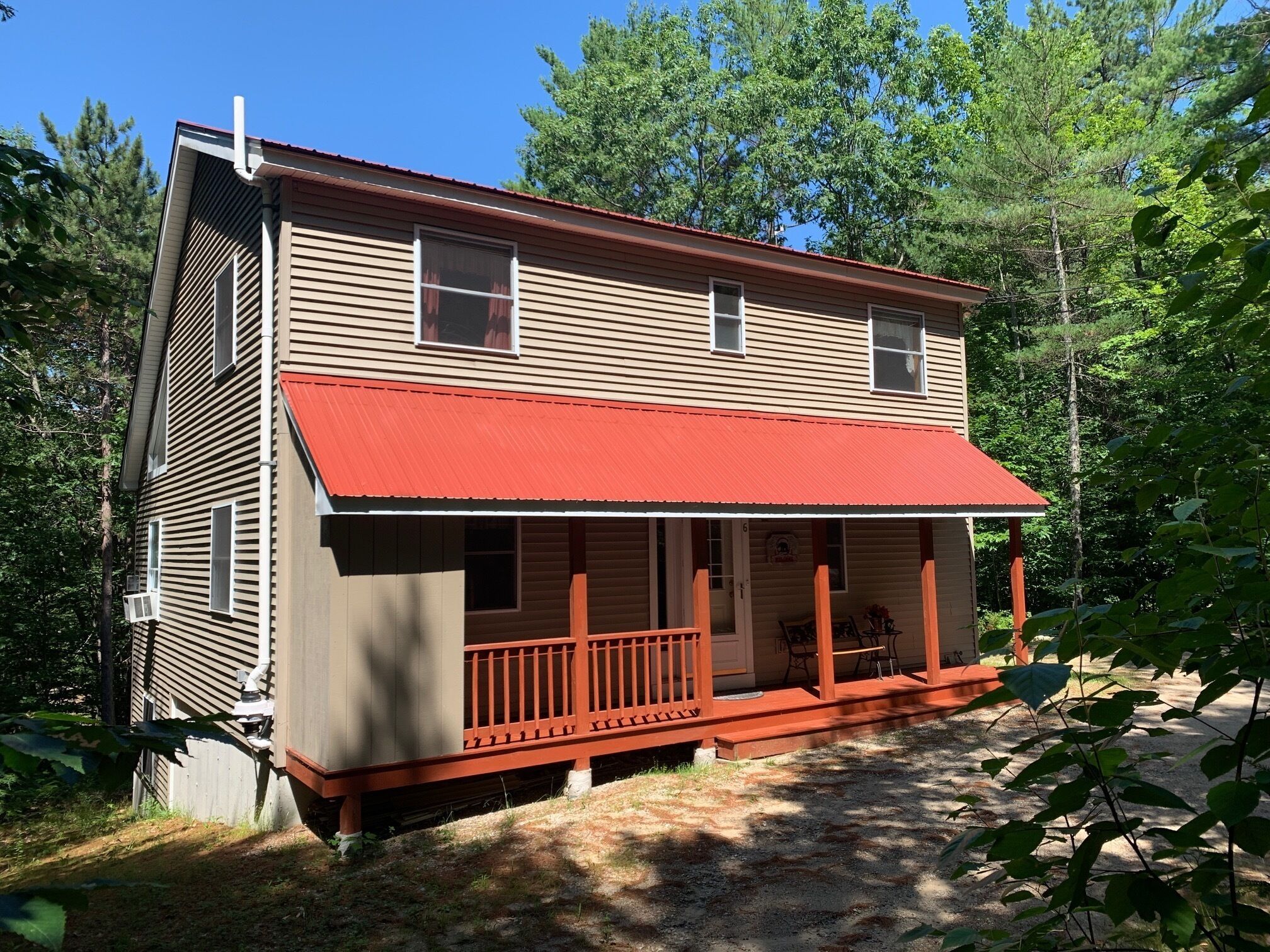 Une cabane en rondins à deux étages, dotée d’un auvent rouge et d’un porche à l’avant.