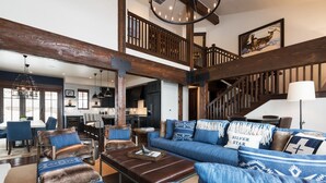 A spacious living area with a large blue sofa set, a brown leather ottoman, and a wooden staircase. - Silver Star 40 | Theater Room | Hot Tub (Park City)