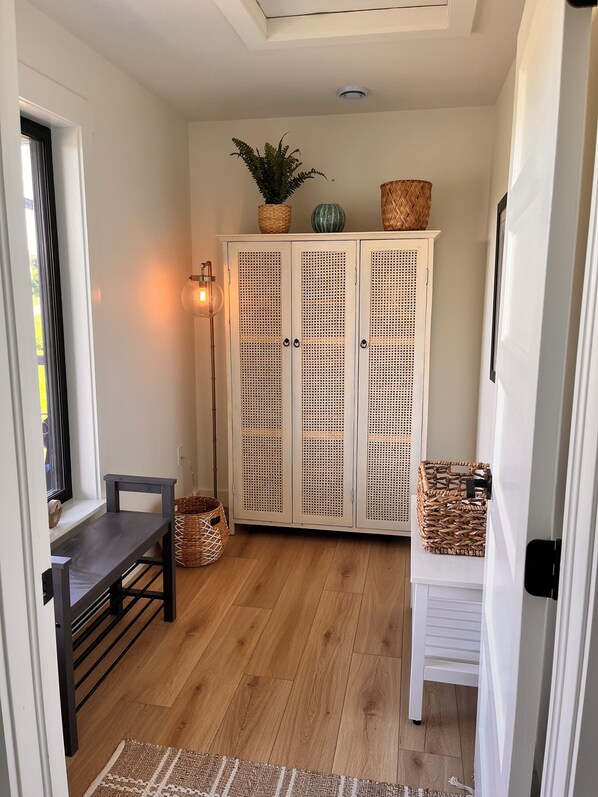 A hallway with a white door, a bench, a wicker basket, and a cabinet with a woven design. - Stunning Modern Beach House: Private, Unblocked Ocean Views in Nova Scotia. (Merigomish, Pictou County)