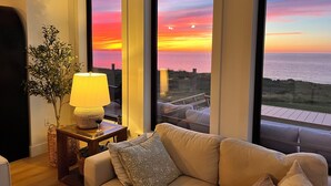 Un salon avec un canapé, une lampe et une vue sur le coucher de soleil sur l’océan.