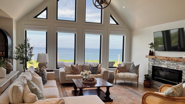 Un salon spacieux avec un haut plafond, de grandes fenêtres donnant sur la mer, une cheminée et des sièges confortables.