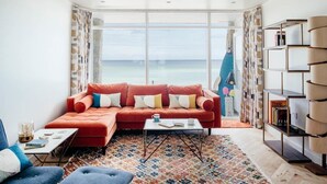 A modern living room with a red sectional sofa, a coffee table, and a view of the ocean. - 6 Barnaloft (St Ives)