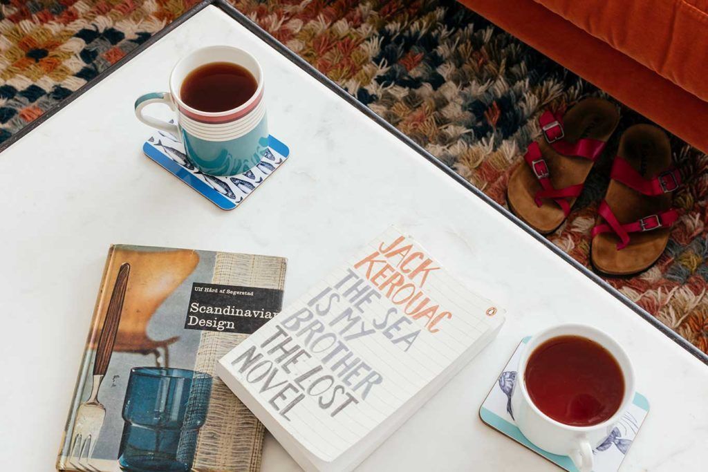 Ein Buch mit dem Titel „Jack Kerouac ist mein Meer“ auf einem weißen Tisch zusammen mit zwei Teetassen und einem Paar Sandalen.